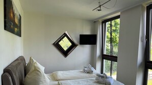 A hotel room with a bed, a window, a flat-screen TV, and a painting on the wall.