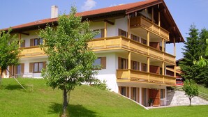 A multi-story hotel with balconies, a sloped roof, and a grassy hill. - Vacation apartment A, 4 pers., panoramic balcony, bedroom, bed-sitting room, 67 sqm (Inzell)