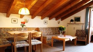 Uma sala de estar aconchegante com teto de madeira, um sofá, uma mesa de jantar com cadeiras e uma mesa de centro.
