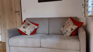 Ein graues Sofa mit roten und gemusterten Kissen, eine Holztür und ein gerahmtes Bild an der Wand.