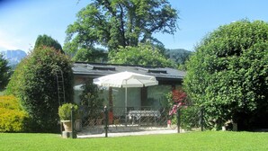 Ein Haus mit überdachter Terrasse, umgeben von üppiger Vegetation und einem Blick auf das Gebirge.