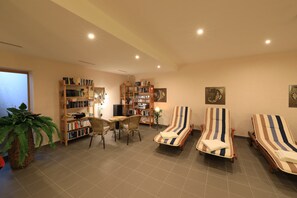 A spacious living area with a bookshelf, a dining table with chairs, and two striped lounge chairs.