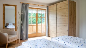 A bedroom with a bed, a chair, a wooden wardrobe, a window with curtains, and a mirror. - Apartment Staufenblick for - 2 persons, 50 sqm, balcony with unobstructed view of the mountains (Bad Reichenhall)