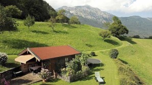 A rustic chalet with a red roof, a patio with seating, and a trampoline, surrounded by lush green fields and mountains in the background. - Apartment Staufenblick for - 2 persons, 50 sqm, balcony with unobstructed view of the mountains (Bad Reichenhall)