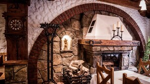 A rustic stone fireplace with a wooden mantel, a clock, and a candle holder. - Hotel KATERAIN (Opava)