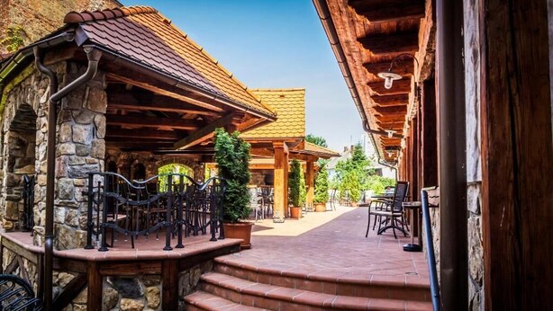 A stone building with a tiled roof, wooden beams, and outdoor seating area with steps leading up to it. - Hotel KATERAIN (Opava)