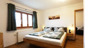 Un lit double avec une literie à motifs, une fenêtre avec des rideaux, un radiateur et une œuvre d’art accrochée au mur.