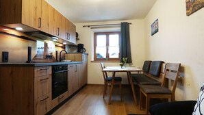 Une cuisine de taille réduite, dotée de meubles en bois, d’une table à manger avec des chaises et d’une fenêtre agrémentée de rideaux.