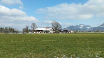 Ein ländliches Anwesen mit einem großen Haus, offenen Feldern und Bergen im Hintergrund.