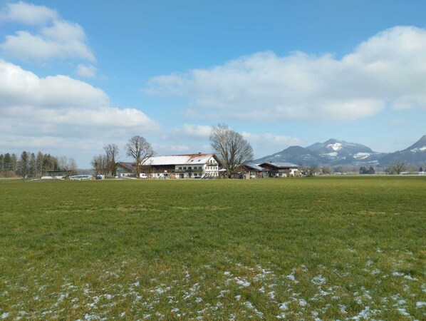 Una propiedad rural con una casa grande, campos abiertos y montañas al fondo.
