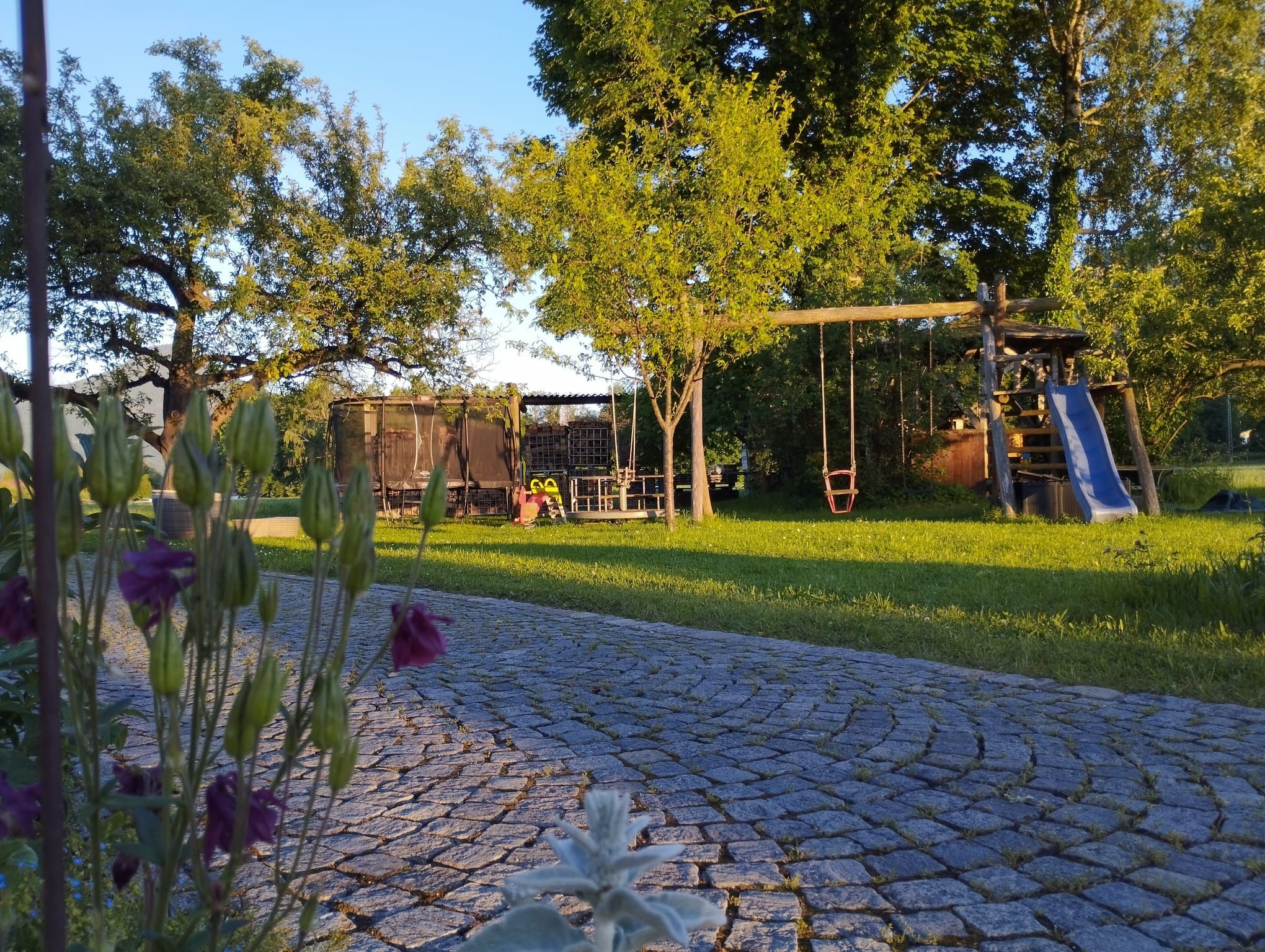 Ein gepflasterter Weg führt zu einem Spielplatz mit Schaukeln und einer Rutsche.
