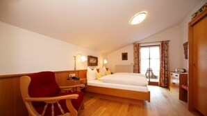 Ein Schlafzimmer mit einem hölzernen Bett, einem roten Sessel, einem Nachttisch und einem Fenster mit Vorhängen.