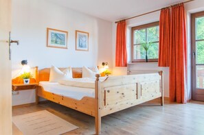 Ein Schlafzimmer mit einem hölzernen Bett, zwei Nachttischen mit Lampen, einem Fenster mit Vorhängen und zwei gerahmten Bildern an der Wand.