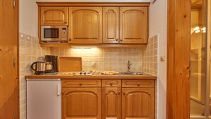 A compact kitchen with wooden cabinets, a microwave, a coffee maker, and a small refrigerator.
