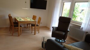 Ein modernes Wohnzimmer mit Essbereich, einem Flachbildfernseher und einem Fenster mit Blick auf Grünflächen.