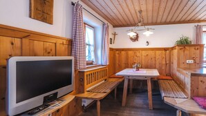 A wooden interior with a television, bench seating, a table, and a cross on the wall. - Ferienwohnung "Wilder Kaiser" im Zuhäusl 72 qm mit drei Schlafzimmer und Balkon° (Sachrang)