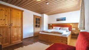 A bedroom with a wooden bed, a wardrobe, and a red chair. - Ferienwohnung "Wilder Kaiser" im Zuhäusl 72 qm mit drei Schlafzimmer und Balkon° (Sachrang)
