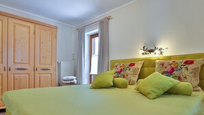 Une chambre à coucher avec un lit, des oreillers verts, un coussin à motifs floraux, une armoire en bois et un radiateur.
