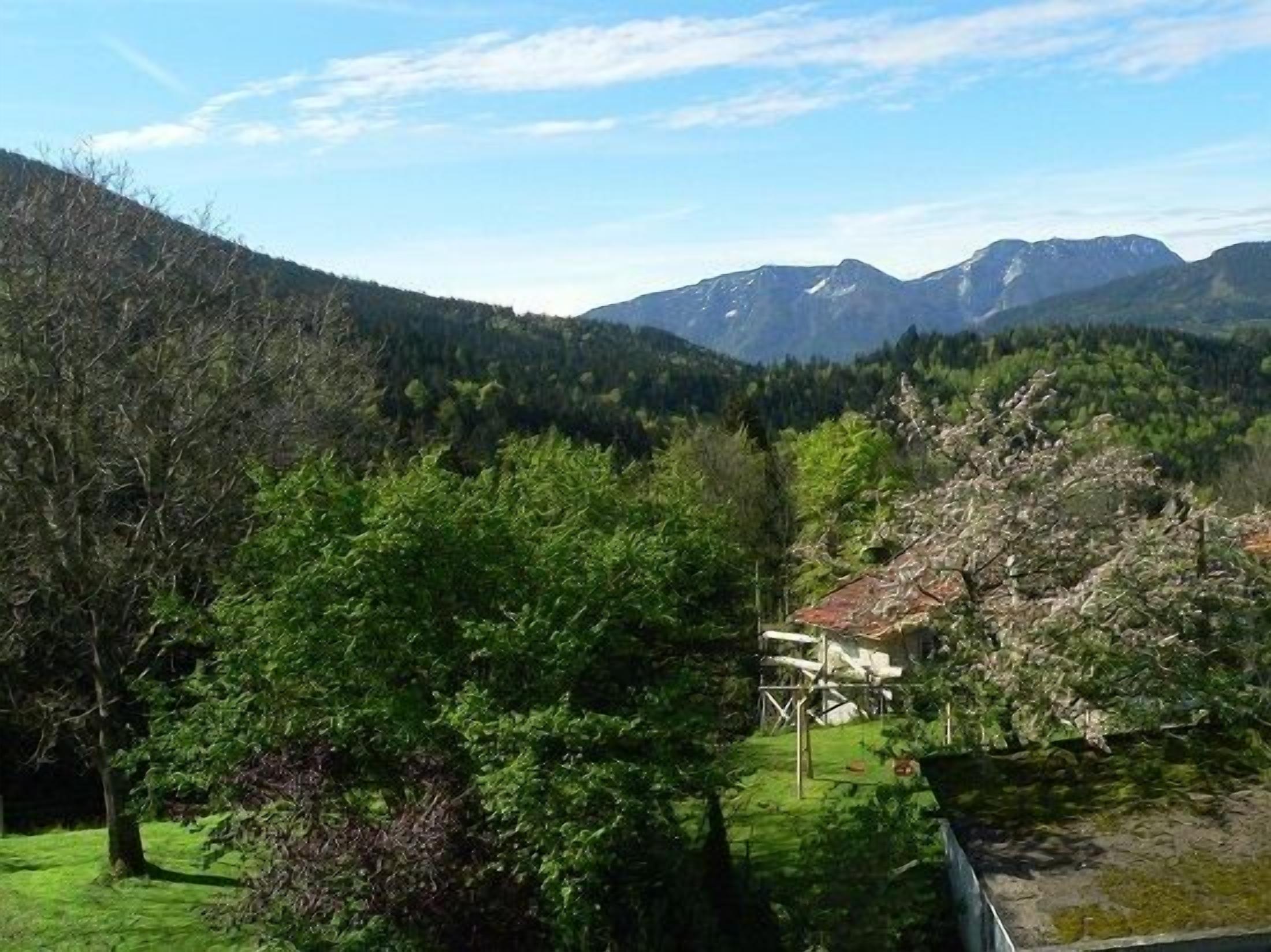 A mountainous landscape with a house surrounded by trees and a clear sky.
