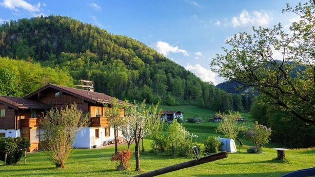 A wooden chalet with a sloped roof, surrounded by a well-maintained garden with various plants and a swing set. - Apartment 2 Comfort for 1-4 pers. (Marktschellenberg)