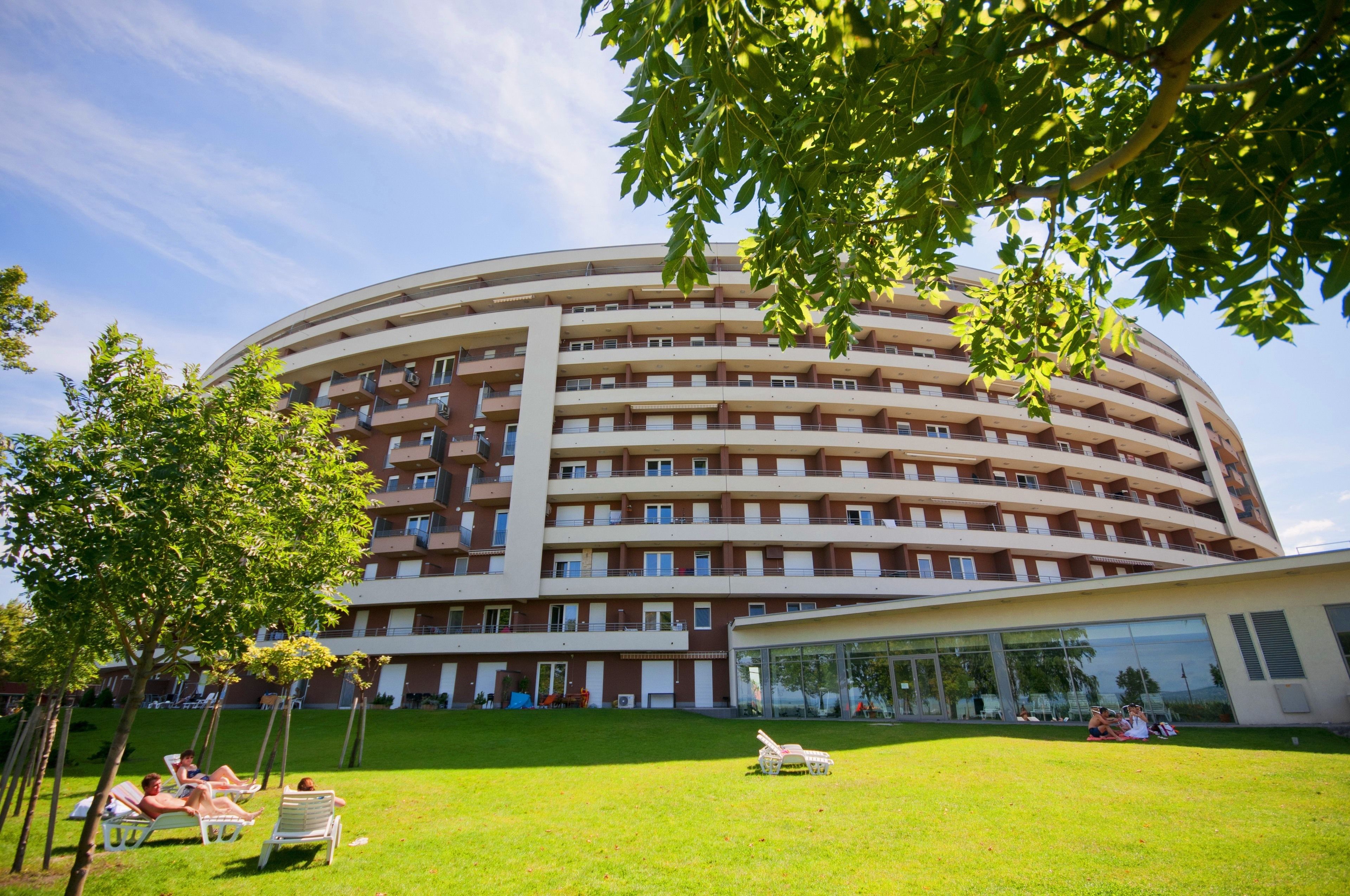 A multi-story hotel with a circular design, outdoor seating area, and a grassy courtyard.