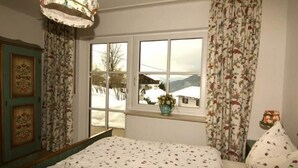A bedroom with a bed, a window with a view of a snowy landscape, and curtains with a floral pattern. - Ferienwohnung Nr.2 für 2-4 Personen (Berchtesgaden)