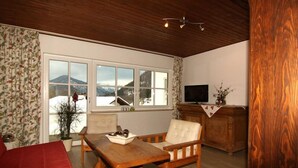 A cozy living room with a wooden table, a sofa, and a TV on a wooden cabinet. - Ferienwohnung Nr.2 für 2-4 Personen (Berchtesgaden)