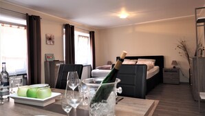 A hotel room with a dining table set for four, a bed with two pillows, a nightstand with a lamp, and a large window with curtains. - Korkenzieher Restaurant Café (Briedel)