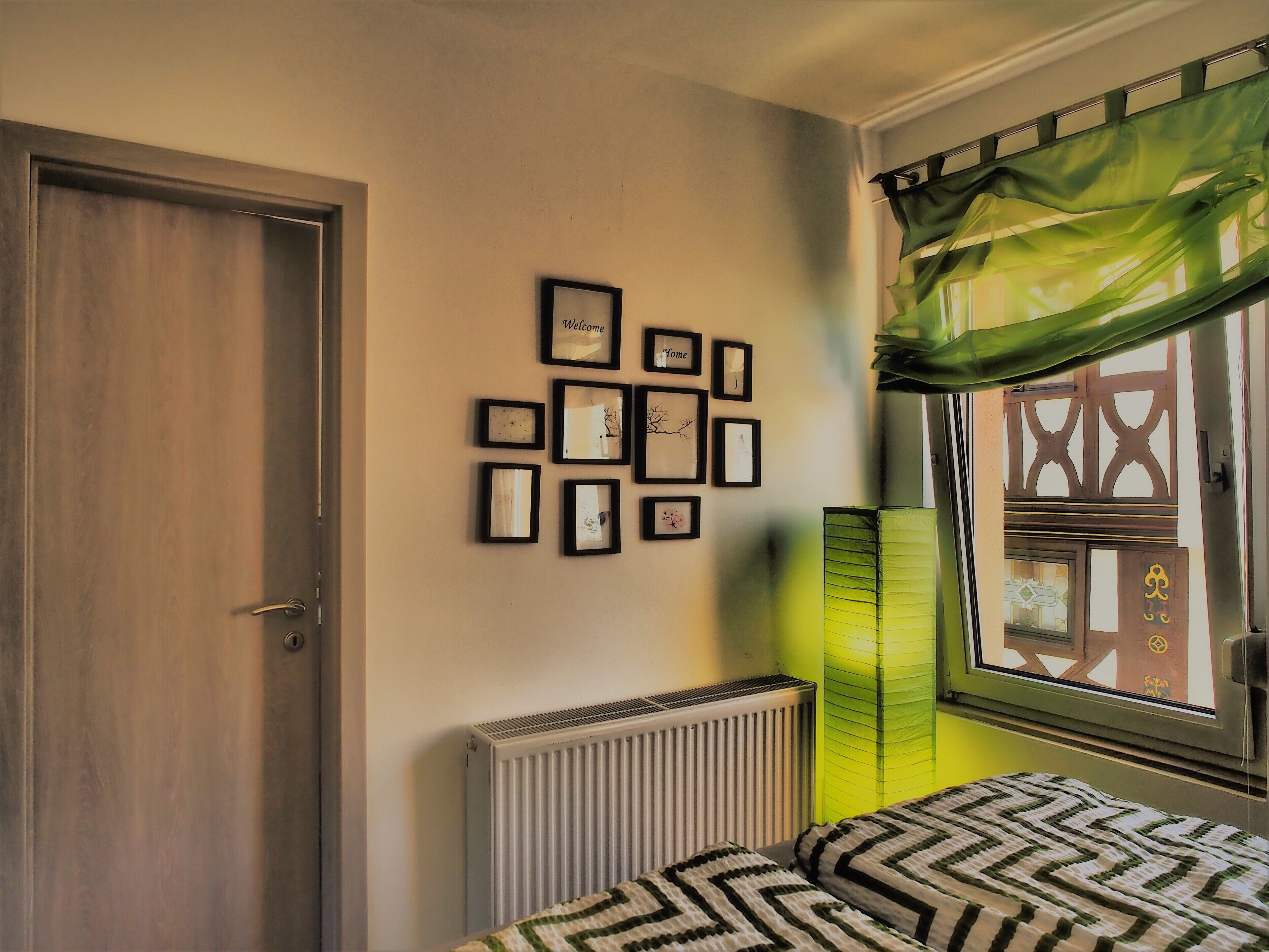 Une chambre à coucher avec un lit, un radiateur, une fenêtre avec un rideau et un mur orné de tableaux.