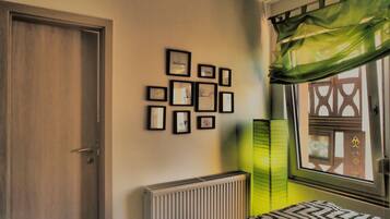 Une chambre à coucher avec un lit, un radiateur, une fenêtre avec un rideau et un mur orné de tableaux.