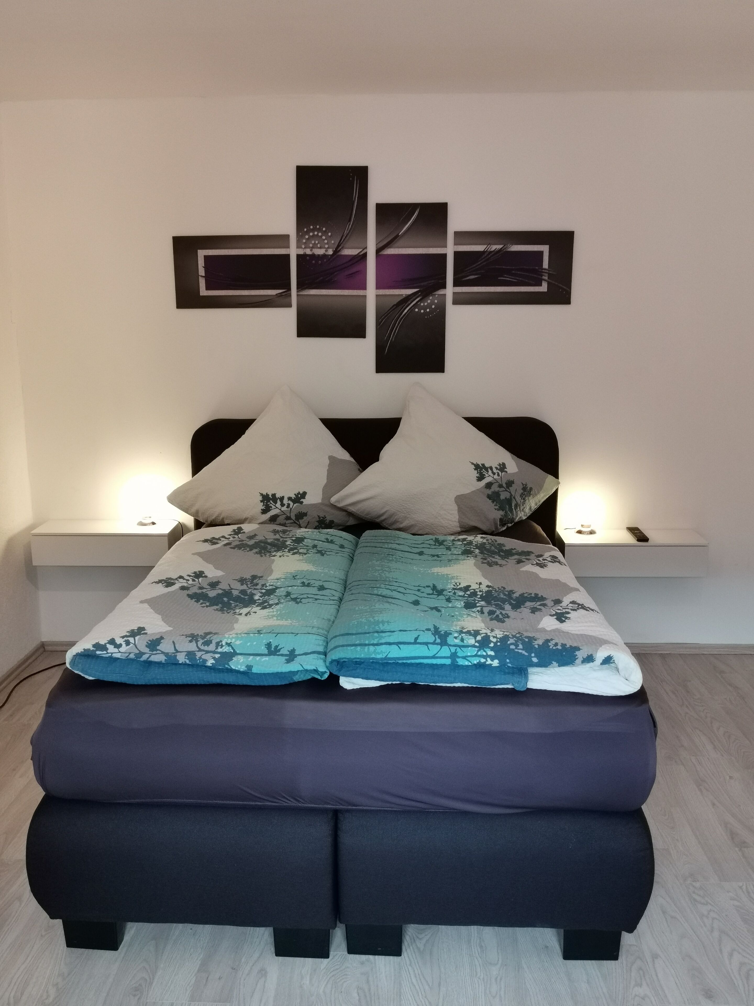 A bedroom with a bed, bedside tables, and wall art.