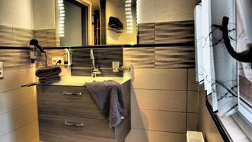 Un baño moderno con tocador con mampara de vidrio, un perchero, un espejo y una ventana con persianas.