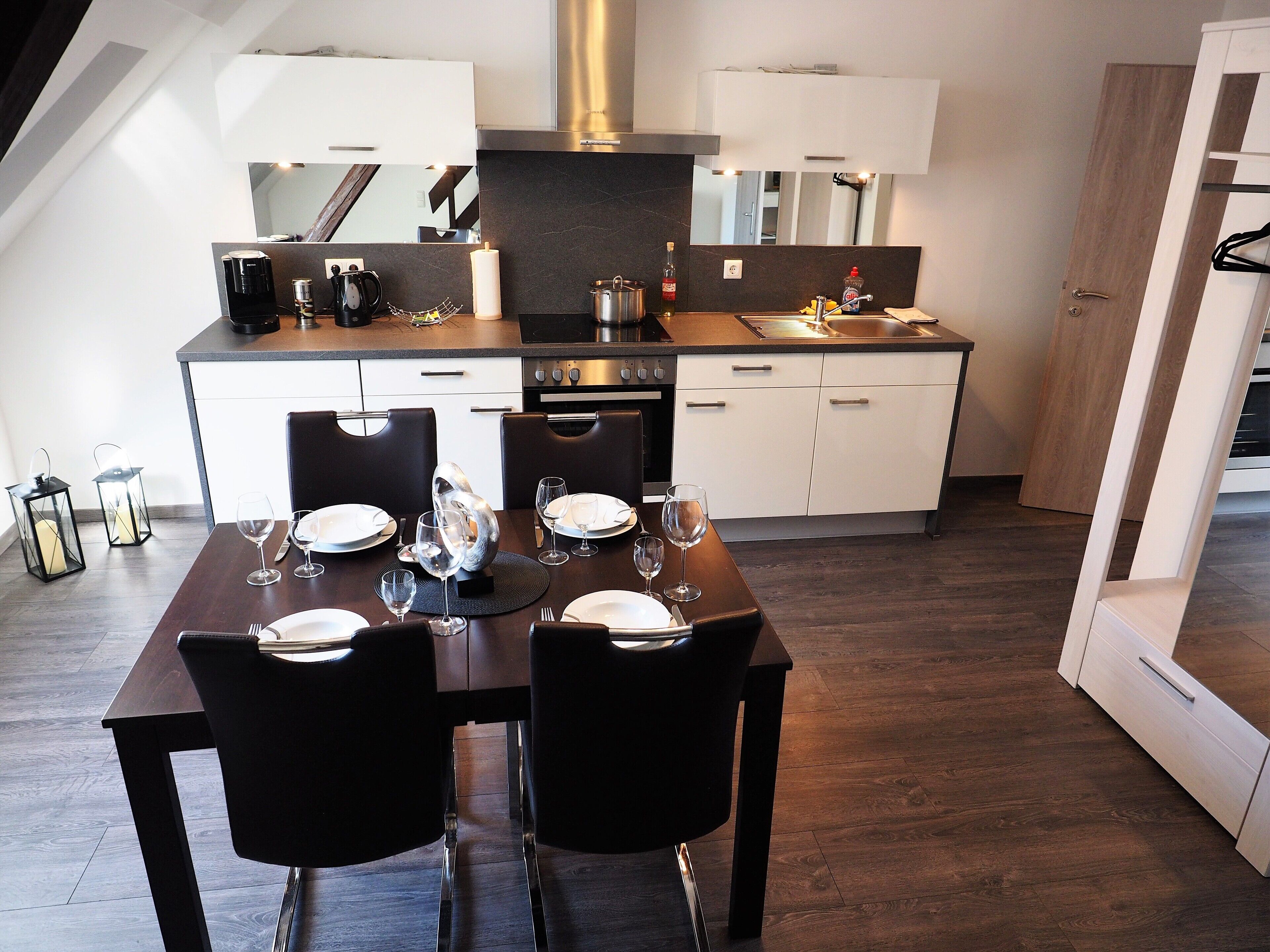 Une cuisine moderne avec un plancher en bois foncé, des armoires blanches et un coin repas aménagé pour deux personnes, avec une table et des chaises.