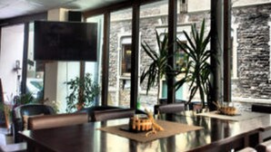 A modern conference room with a large table, comfortable seating, a flat-screen TV, and large windows with a view of a stone wall. - Korkenzieher Restaurant Café (Briedel)
