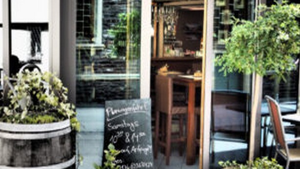 A restaurant entrance with a chalkboard menu, outdoor seating, and potted plants. - Korkenzieher Restaurant Café (Briedel)