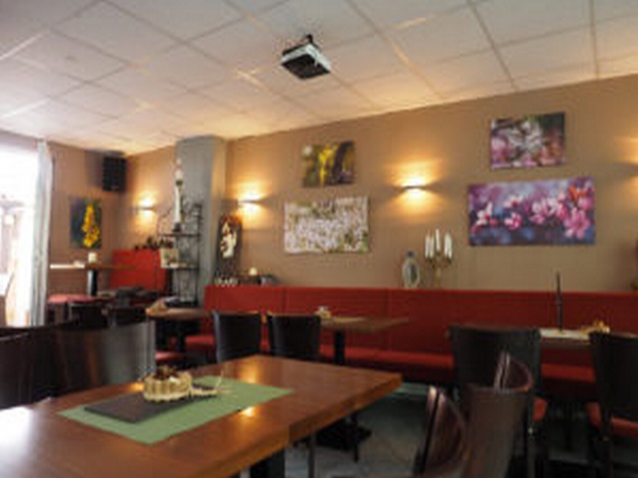 Ein Restaurant mit einem langen Holztisch, roten Sitzgelegenheiten und Wandbildern.
