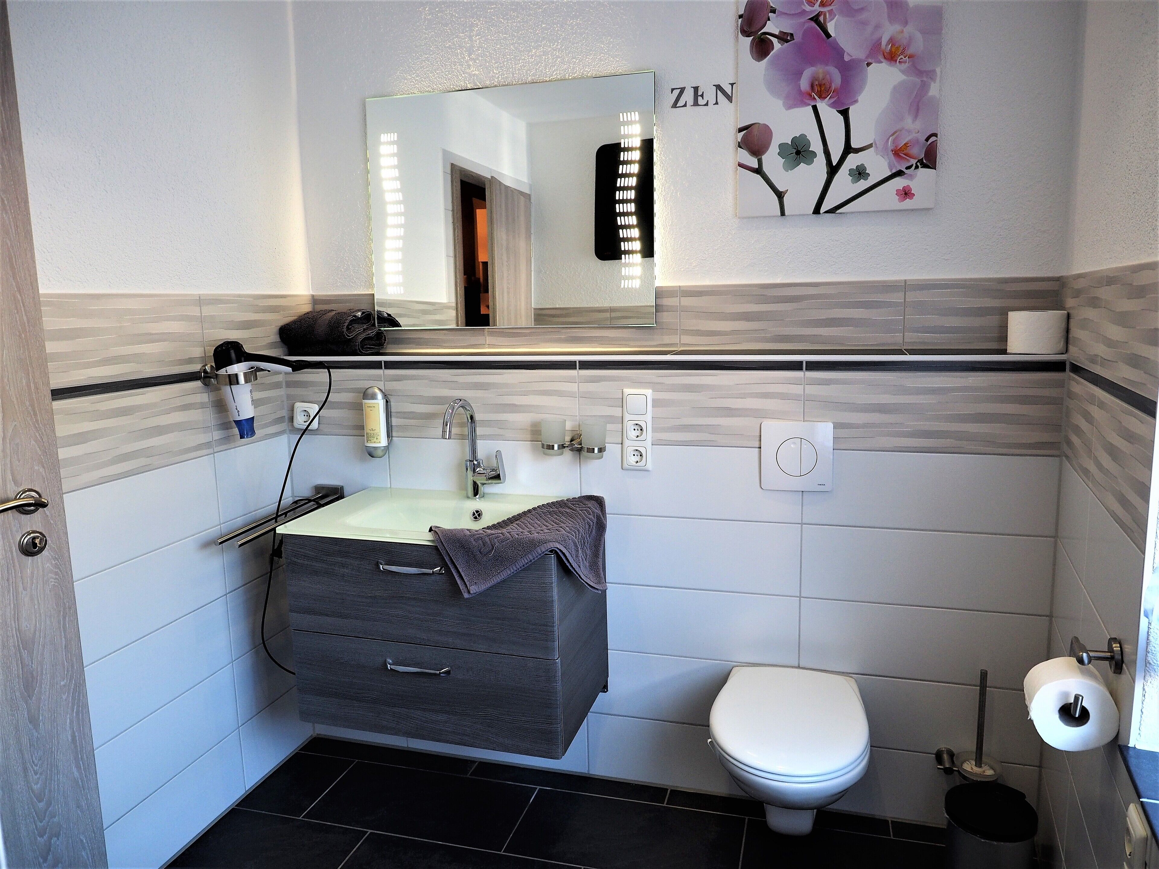 Un bagno moderno con un mobile lavabo grigio, un water bianco e uno specchio sopra il lavandino.