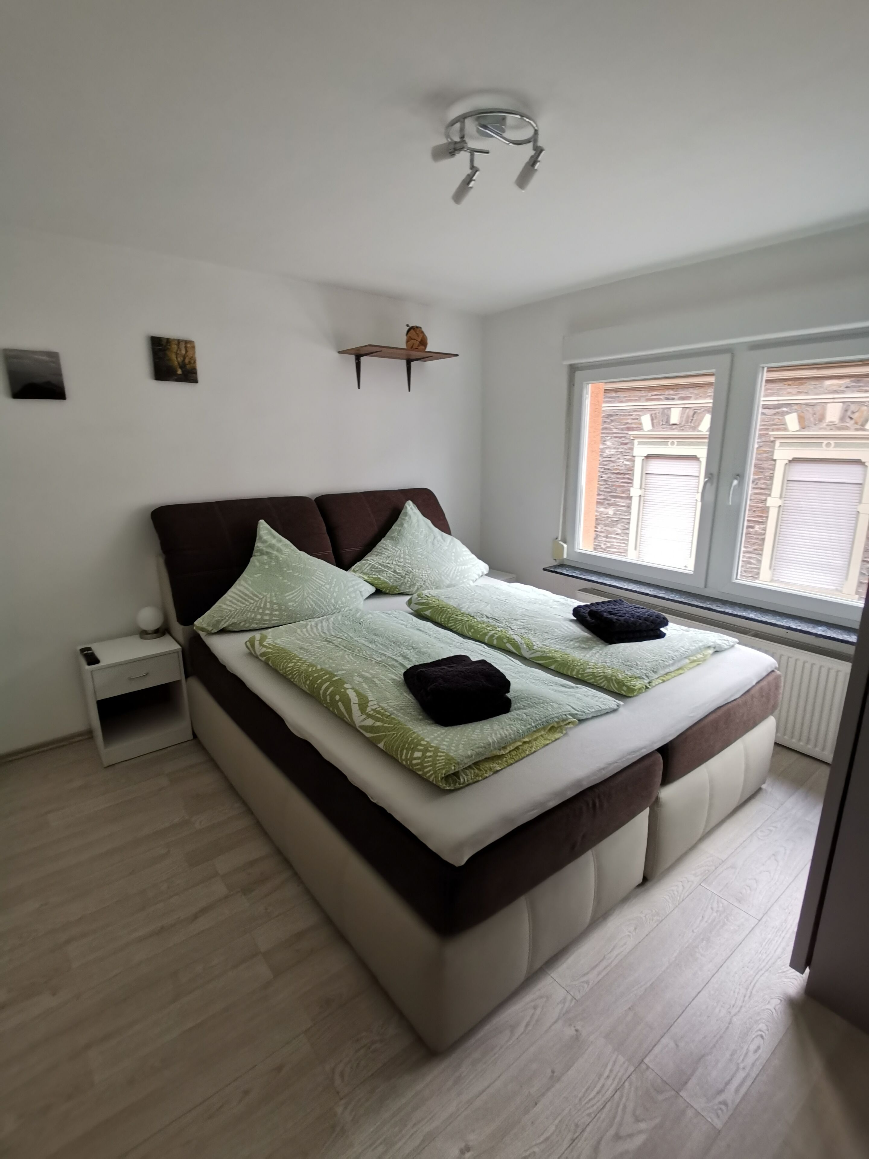 Een slaapkamer met een bed, nachtkastje en een raam met luiken.