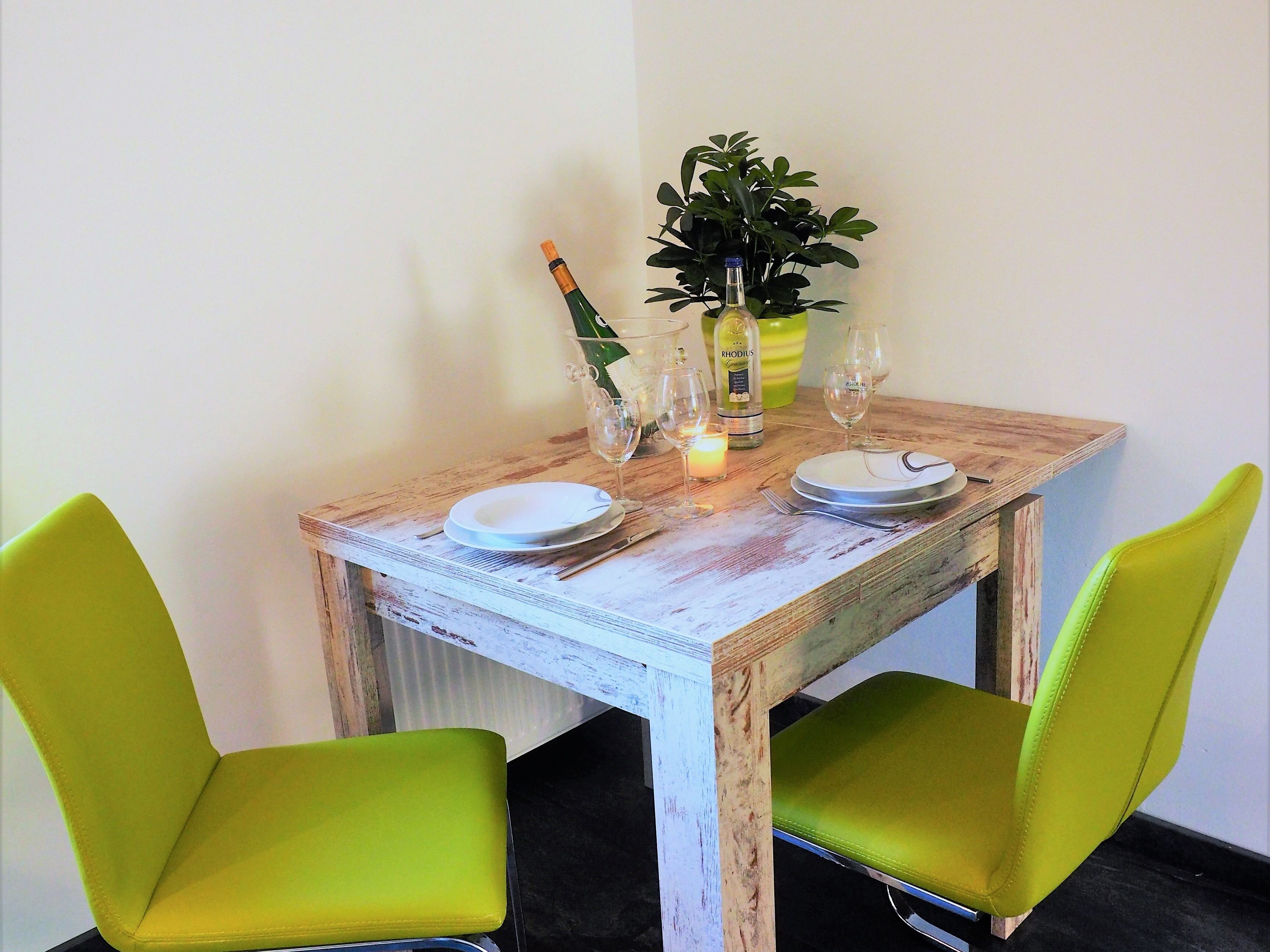 A dining table with two green chairs, a candle, wine glasses, and a bottle of Rhodius.