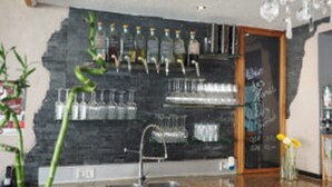 A kitchen with a stone backsplash, a sink, and a bar area with shelves of glassware. - Korkenzieher Restaurant Café (Briedel)
