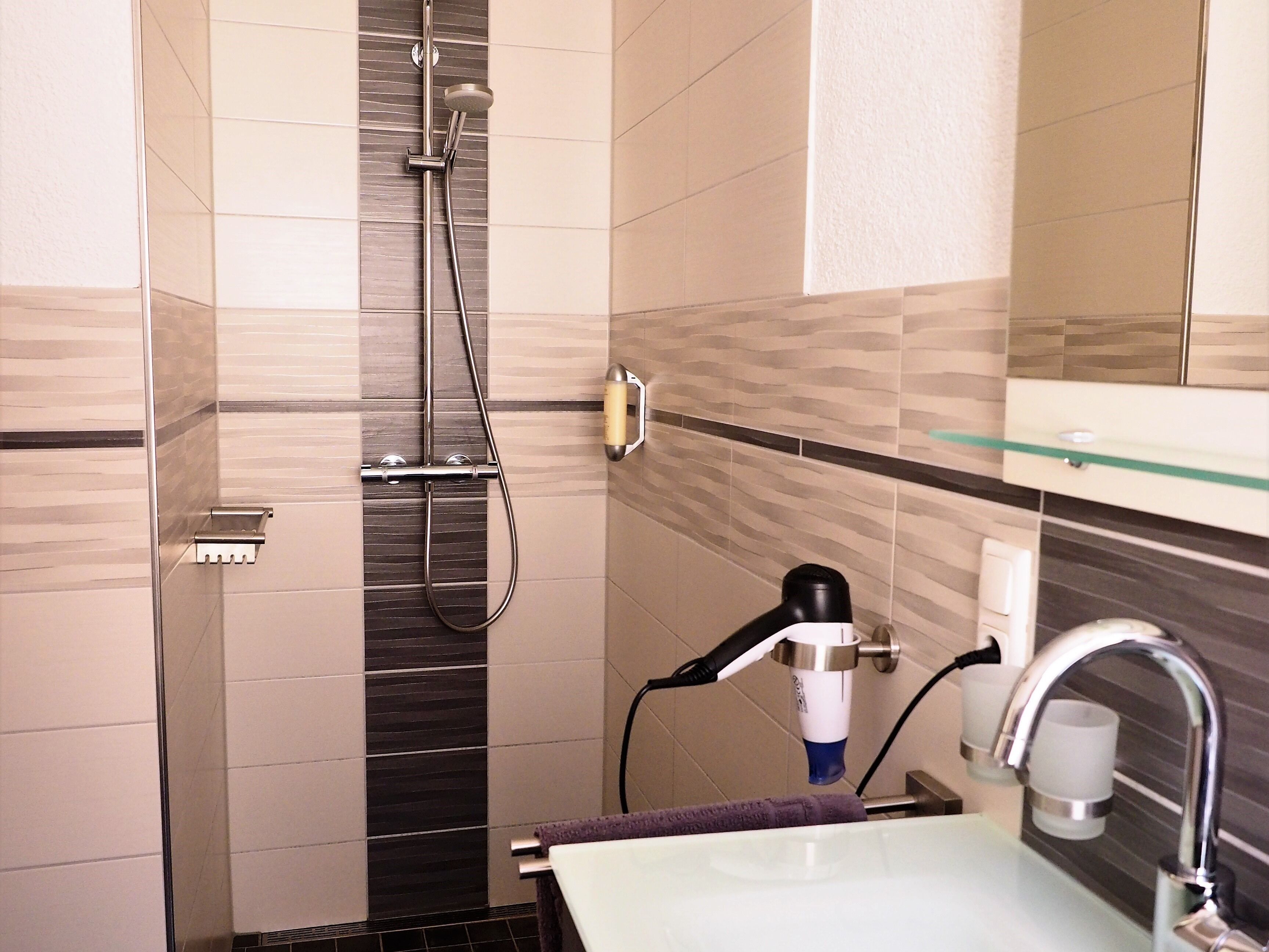 Un baño con ducha, lavamanos y secador de pelo.