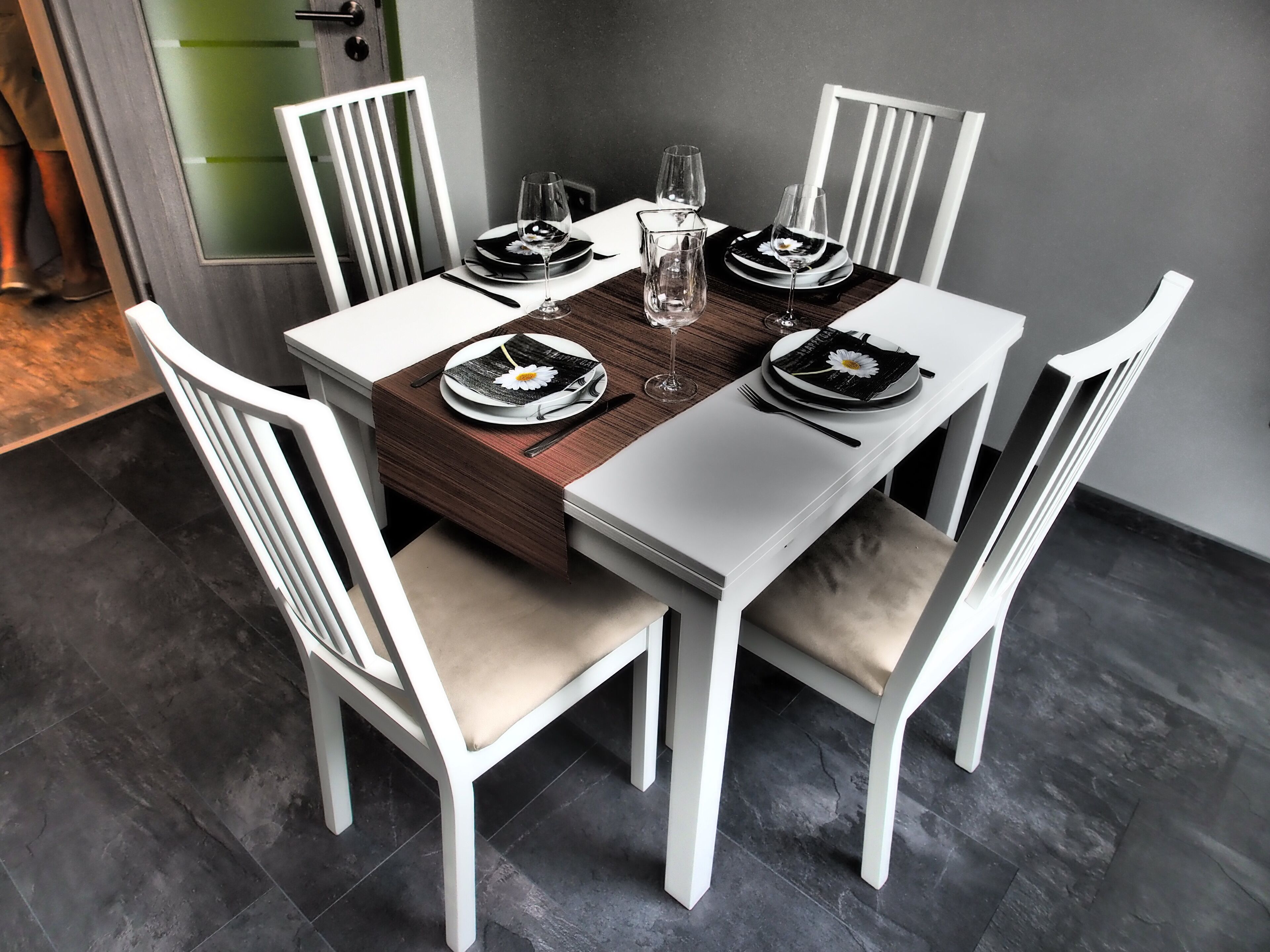A dining table set with plates, cutlery, and glasses, surrounded by white chairs with cushioned seats.