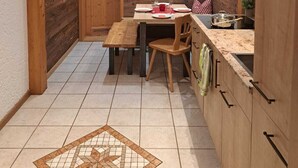 A compact kitchen with wooden cabinets, a dining table with chairs, and a tiled floor.