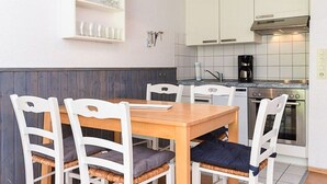 A compact kitchen with white cabinets, a wooden dining table, and a built-in oven. - Holiday house North Sea Mermaid (Esens)