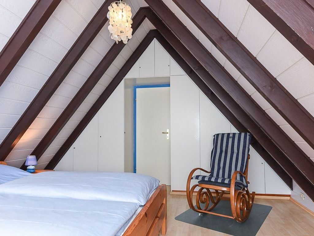 A bedroom with a sloped ceiling, a bed, a rocking chair, and a door.