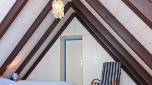 A bedroom with a sloped ceiling, a bed, a rocking chair, and a door. - Holiday house North Sea Mermaid (Esens)