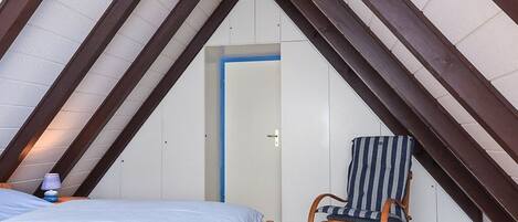 A bedroom with a sloped ceiling, a bed, a rocking chair, and a door.