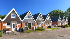 A row of modern, single-story houses with pitched roofs, a paved driveway, and a clear blue sky. - Holiday house North Sea Mermaid (Esens)