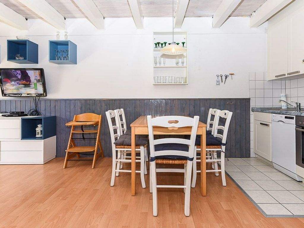 A compact kitchen with a dining area, wooden chairs, a TV, and a shelf with glassware.