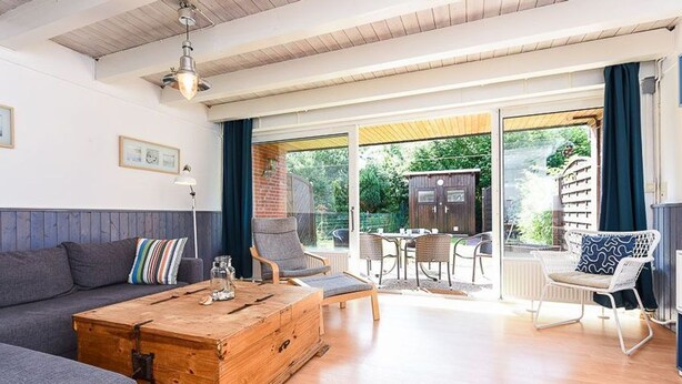 A modern living room with a sofa, a wooden coffee table, and a dining area with chairs and a table. - Holiday house North Sea Mermaid (Esens)